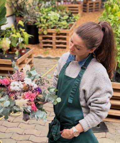 Plantula Amedorf - Lisa Jordan Inhaberin Frau mit einem Strauß aus bunten Blumen in einem Gewächshaus.
