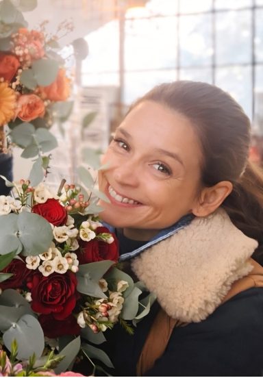 Plantula Amedorf - Lisa Jordan Inhaberin Lächelnde Frau hält einen Blumenstrauß mit roten und weißen Blumen in der Hand.